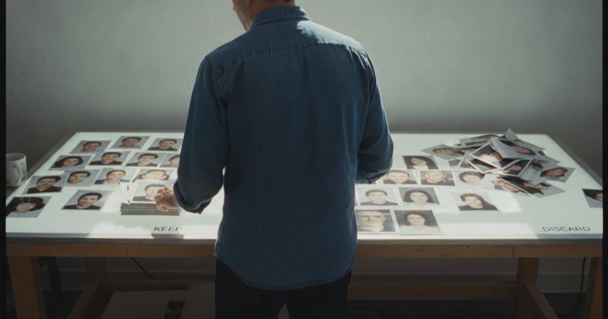 An ordinary person at a light table sorting through many printed photos, keeping some and discarding others