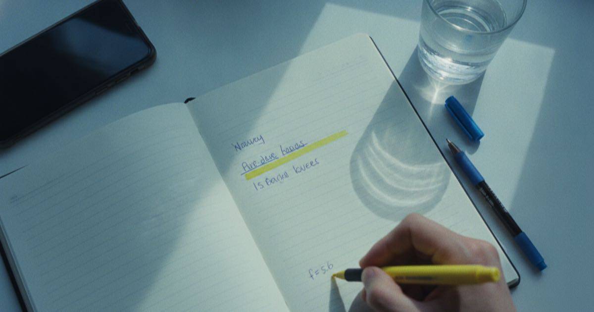 Overhead view of a notebook with short handwritten bio drafts on a desk